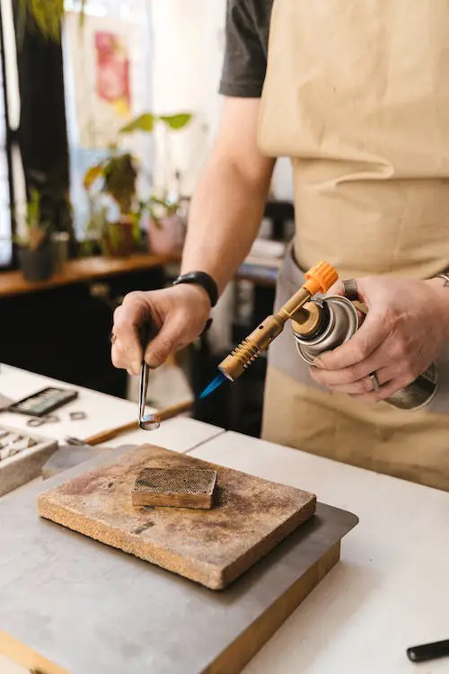 Artisan jeweler using a torch to work on a metal piece over a heat-resistant block