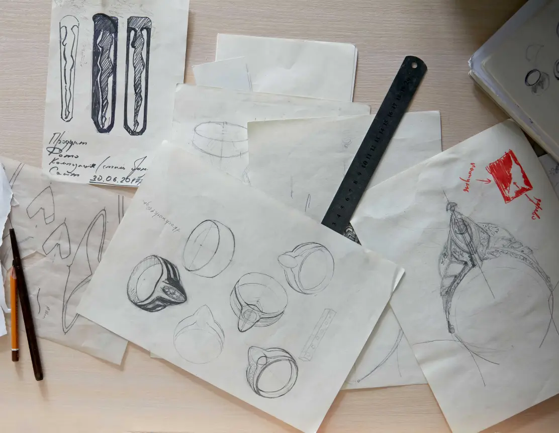 Sketches of jewelry designs on a desk with drawing tools and measurement ruler